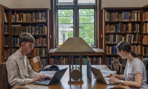 Two students sat on laptops in a library